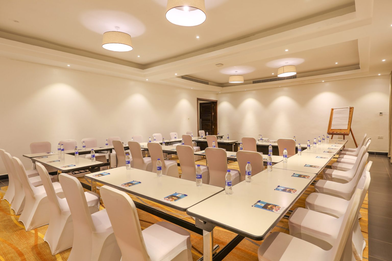 A meeting room laid out in a U-shape with covered chairs, bottled water on the tables and a flip chart in the corner.
