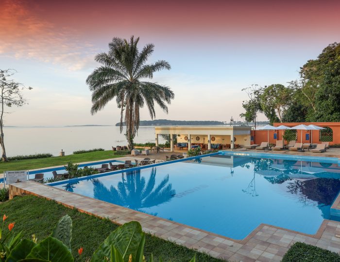 A large swimming pool beside Lake Victoria at first light, with a tall palm, a poolside bar and loungers.