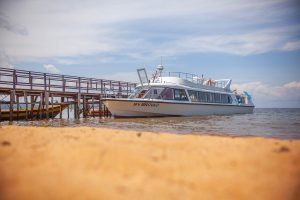 Seen low over golden sand, the MV Brovad lies alongside a wooden jetty on the lake under a bright blue sky.