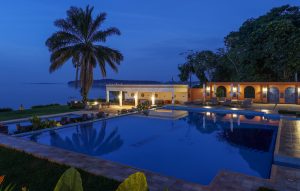 The swimming pool at blue hour, lit from within, with the open-sided poolside bar glowing and Lake Victoria behind.