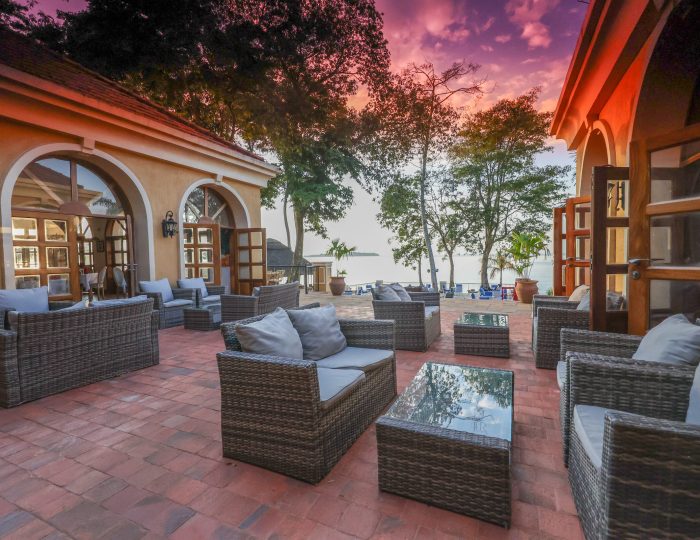 Wicker sofas on a brick terrace outside arched doors, with a pink sunset sky over the lake beyond.